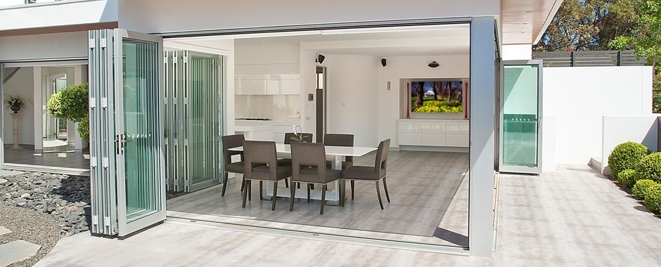 Aluminium bi-fold doors opening up a dining area on two sides with dining table in centre